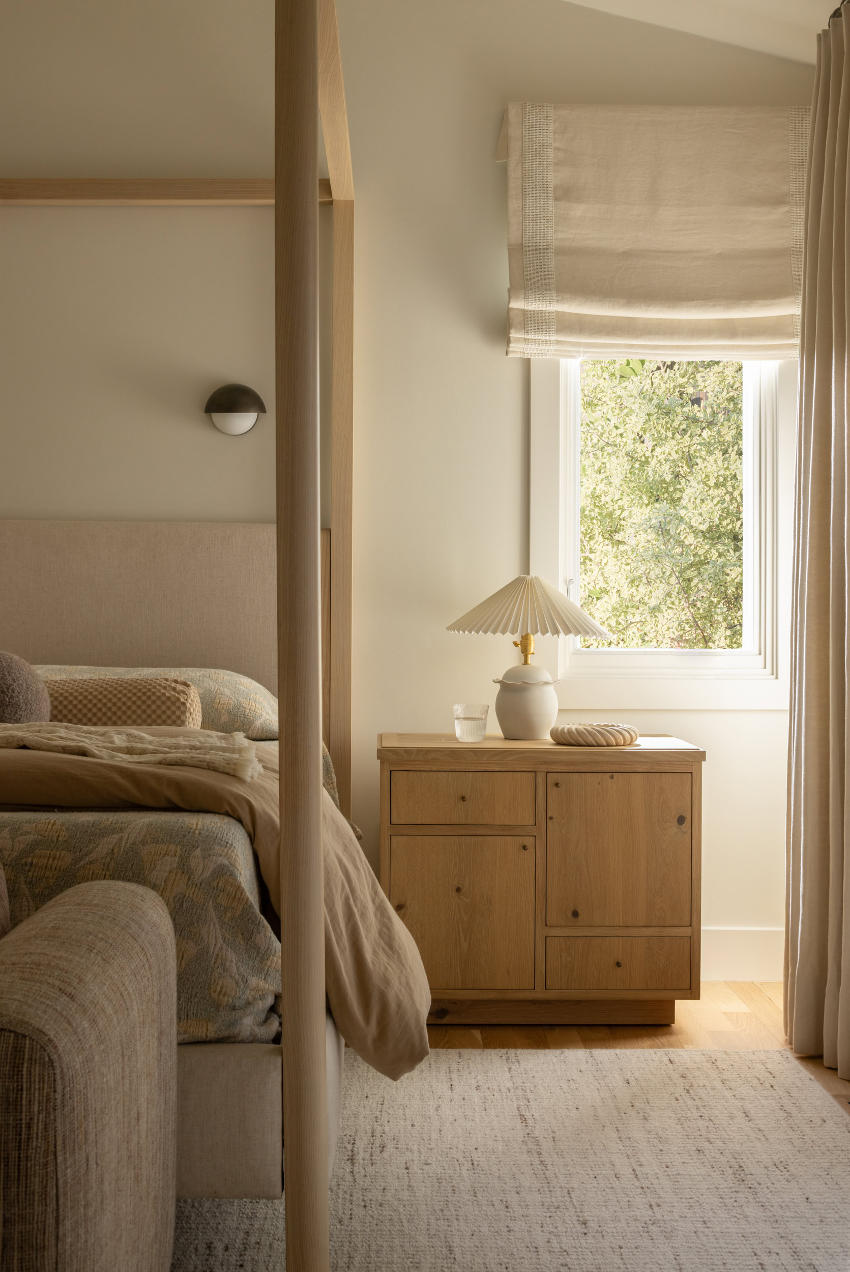Bright bedroom with neutral tones, wooden furniture, and large window overlooking greenery.
