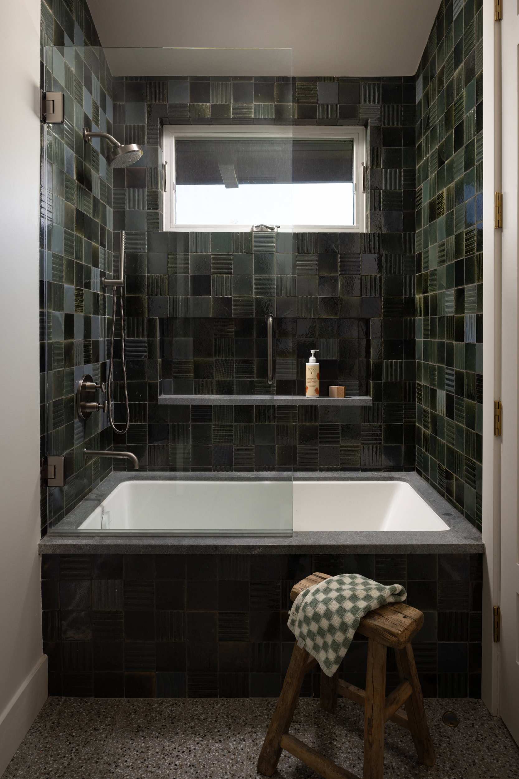 Stylish black tiled bathroom with bathtub and window.