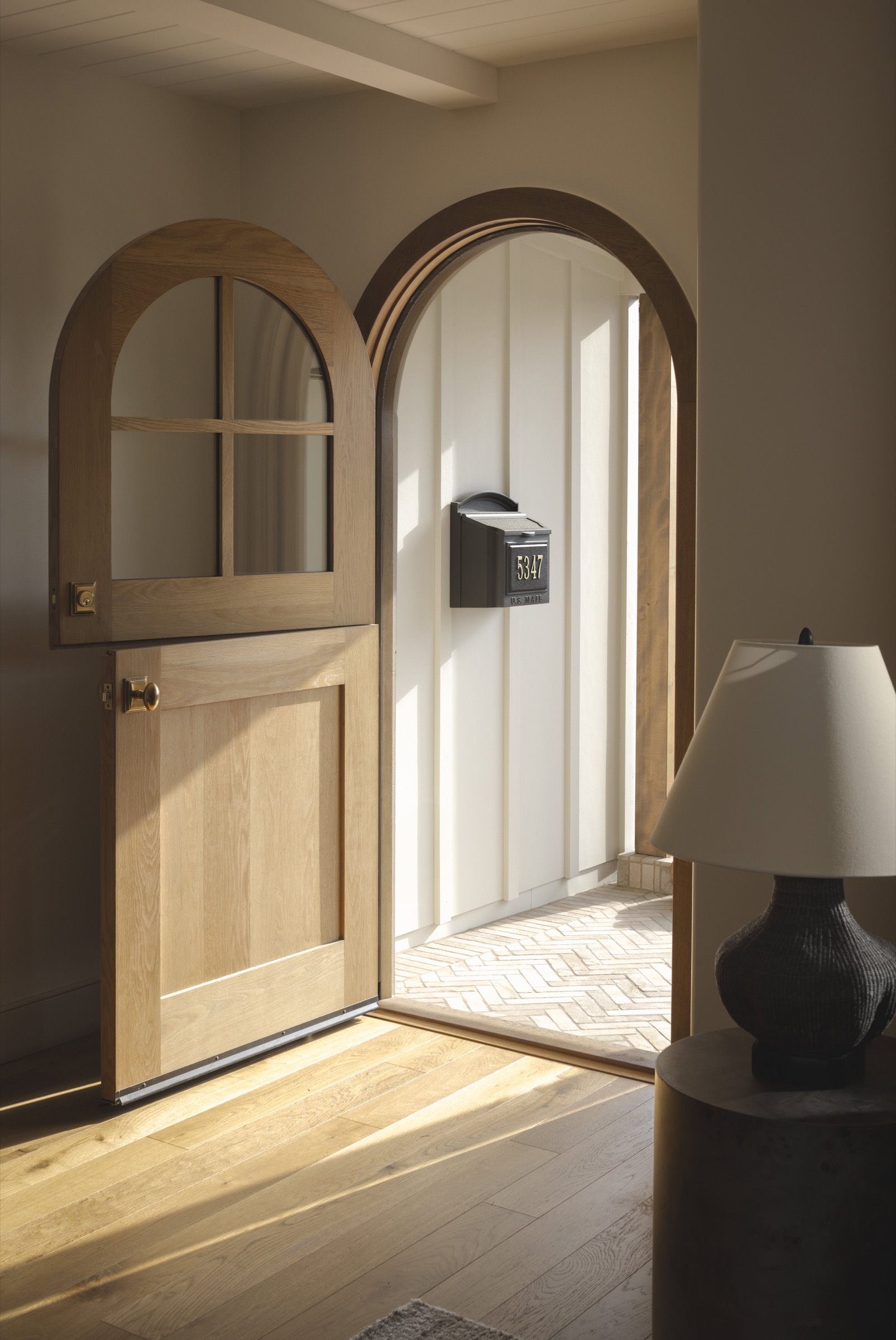Elegant wooden arch door leading to the hallway, featuring a mailbox and natural light.