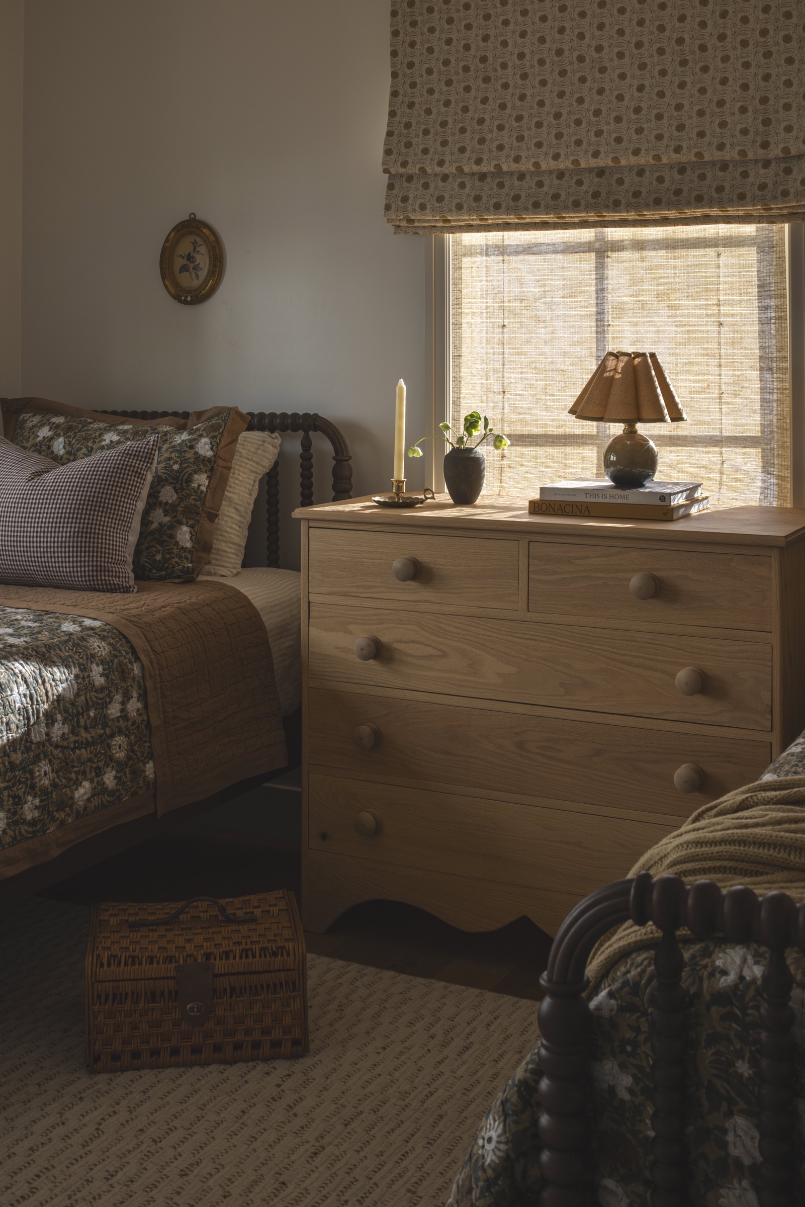 Warm bedroom with wooden dresser, cozy bedding, and natural light from window.