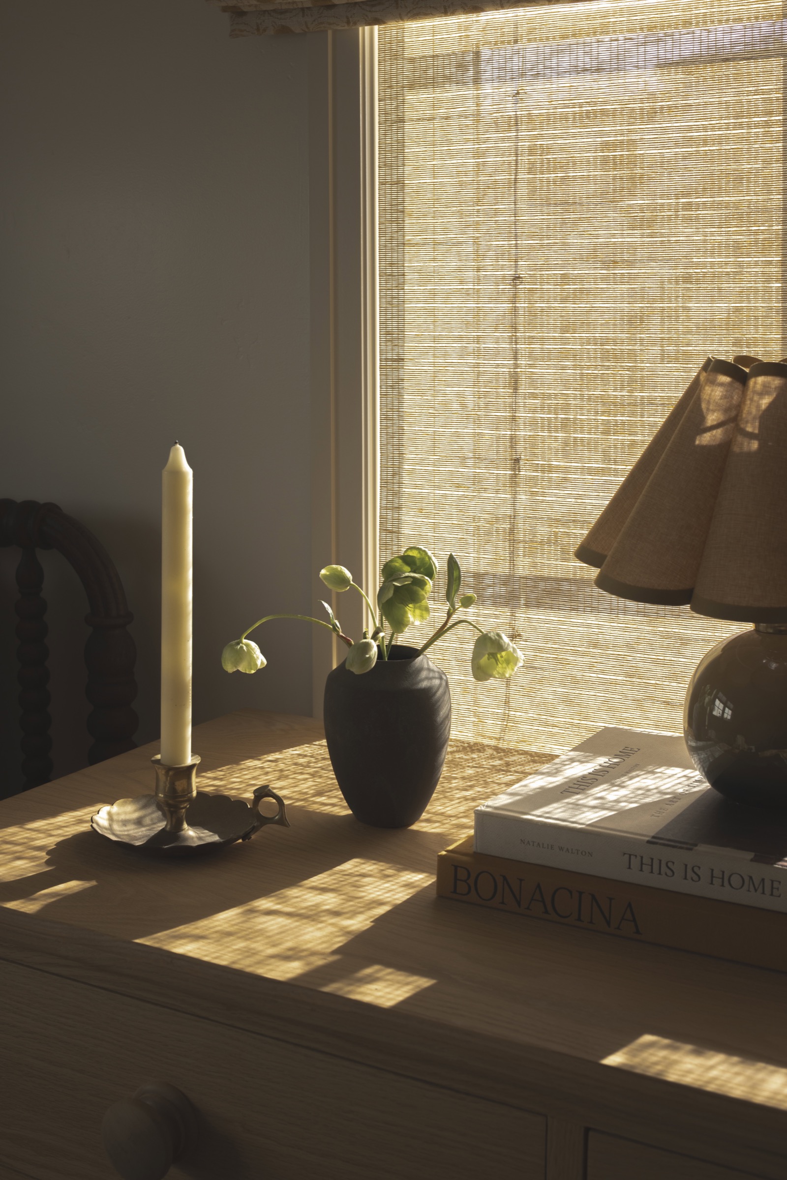 Sunlit interior featuring a vase with green plants, a candle, and a table lamp, creating a warm and.