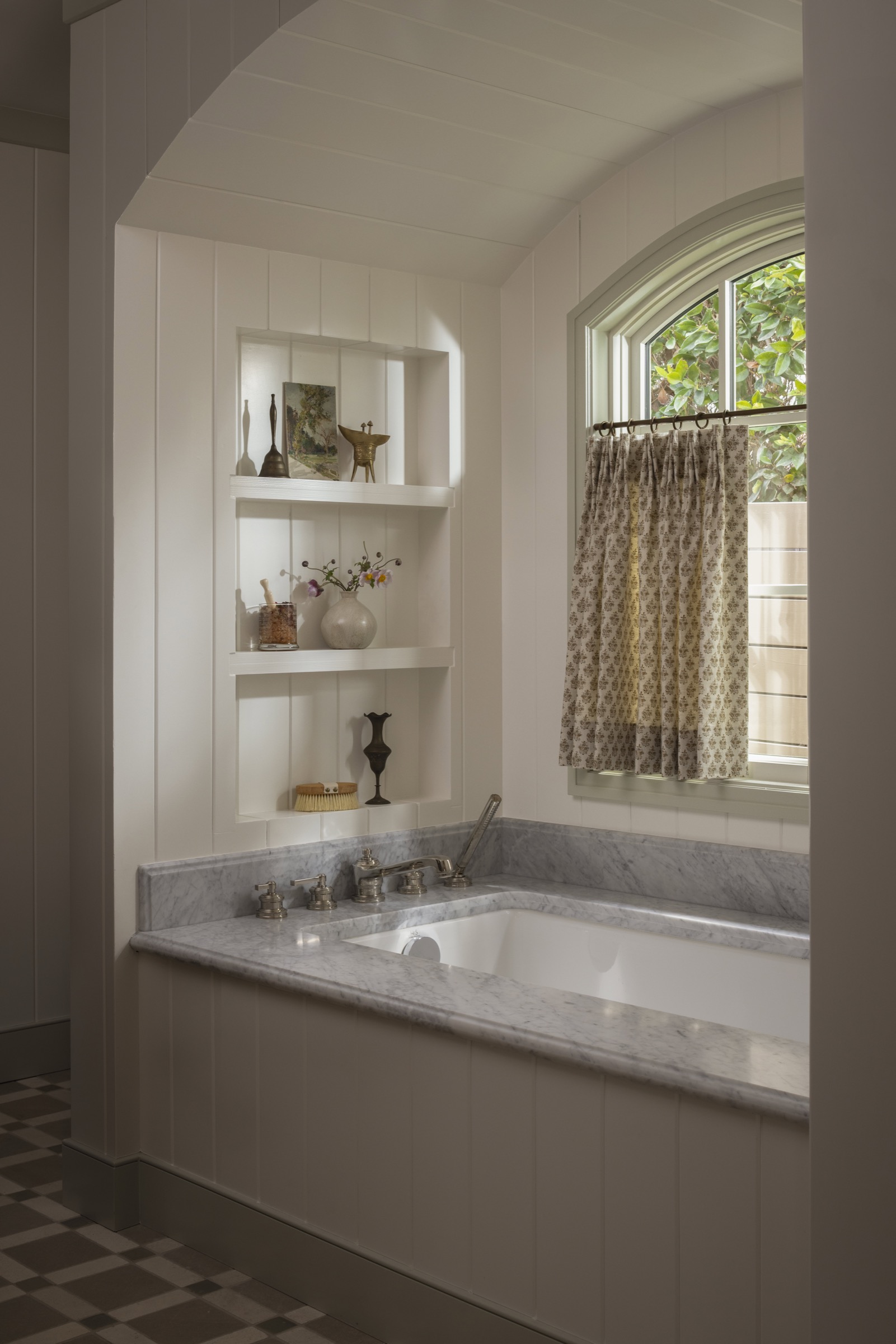 Bathroom with built-in white shelves and a large window with patterned curtains.