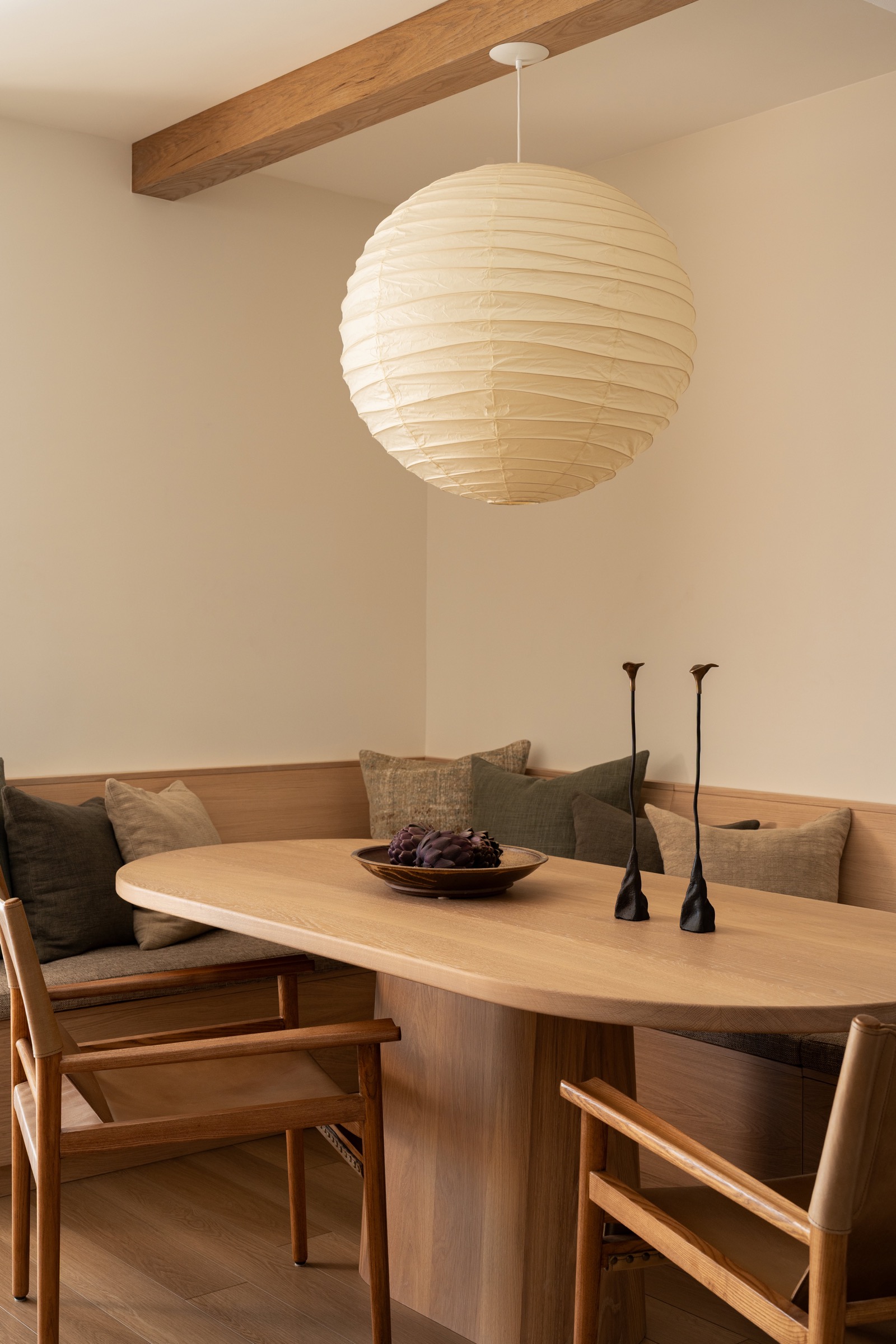 Elegant dining area featuring a round wooden table, cozy seating, and a large paper lantern pendant.