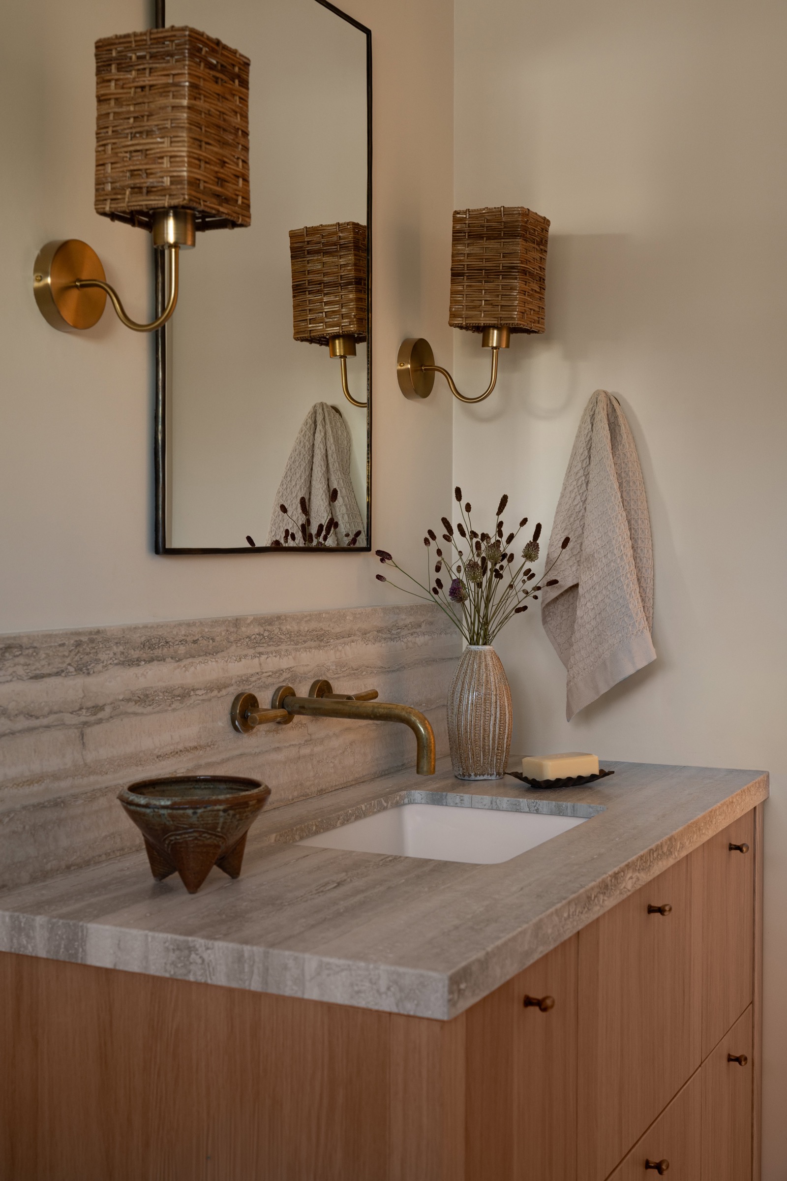 Elegant bathroom vanity with wicker wall sconces and decorative vase.